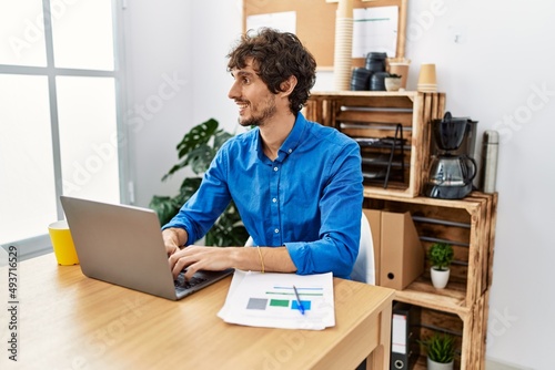 Young hispanic man with beard working at the office using computer laptop looking away to side with smile on face, natural expression. laughing confident.