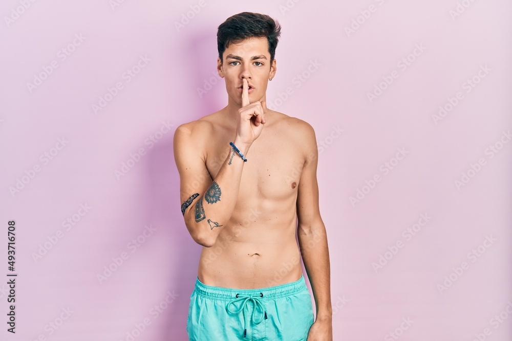 Fototapeta premium Young hispanic man wearing swimwear shirtless asking to be quiet with finger on lips. silence and secret concept.
