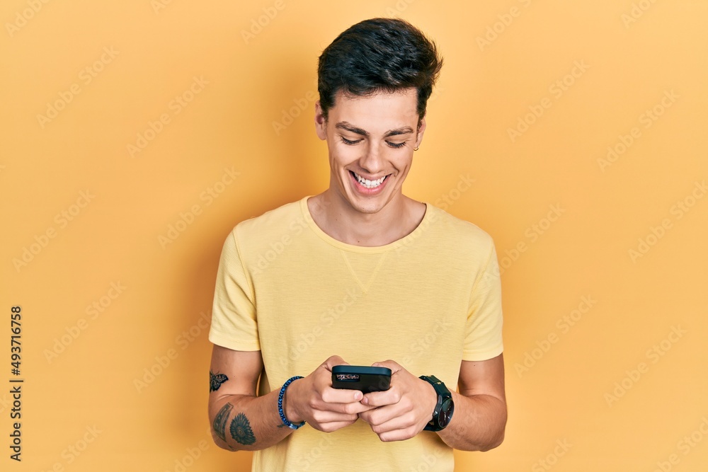 Young hispanic man using smartphone typing message smiling and laughing hard out loud because funny crazy joke.