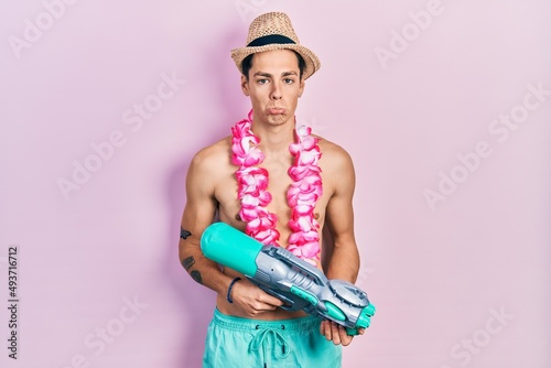 Young hispanic man wearing swimsuit and watergun depressed and worry for distress, crying angry and afraid. sad expression. photo