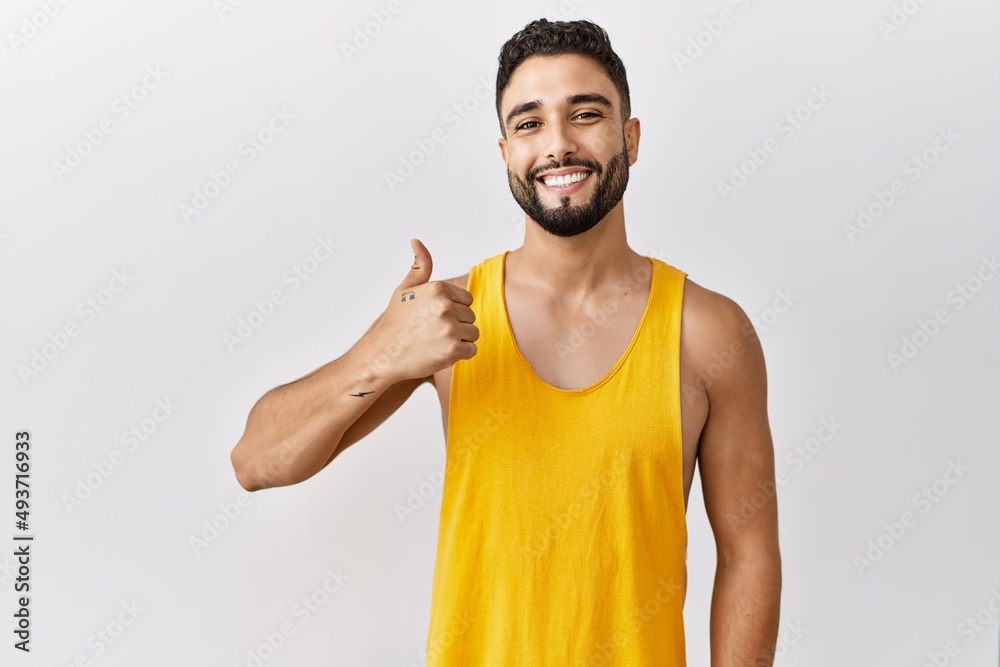 Young handsome man with beard standing over isolated background doing happy thumbs up gesture with hand. approving expression looking at the camera showing success. Young handsome man with beard standing over isolated background doing happy thumbs up gesture with hand. approving expression looking at the camera showing success.