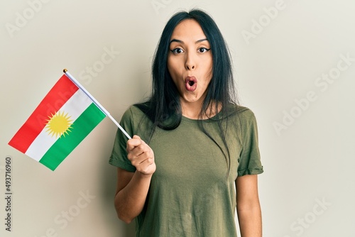 Young hispanic girl holding kurdistan flag scared and amazed with open mouth for surprise, disbelief face photo