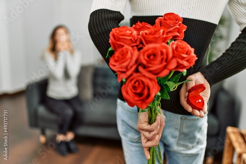 Man suprising woman with bouquet of roses and engagement ring at home. photo