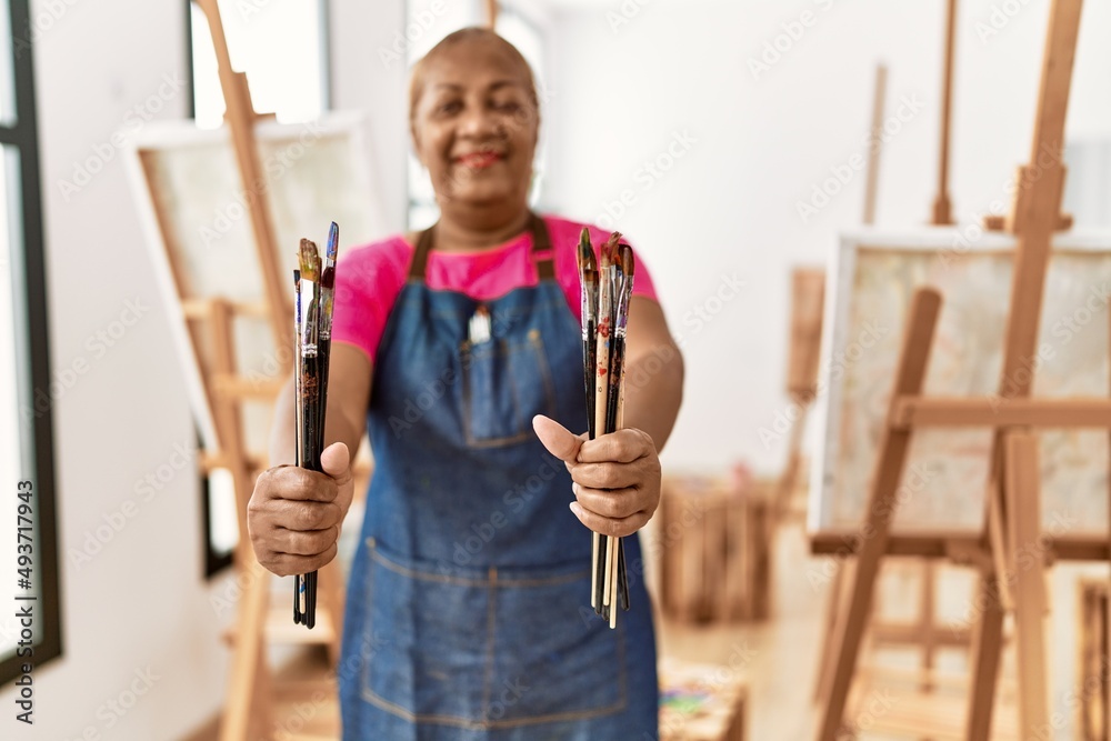 Senior african american woman smiling confident holding paintbrushes at art studio