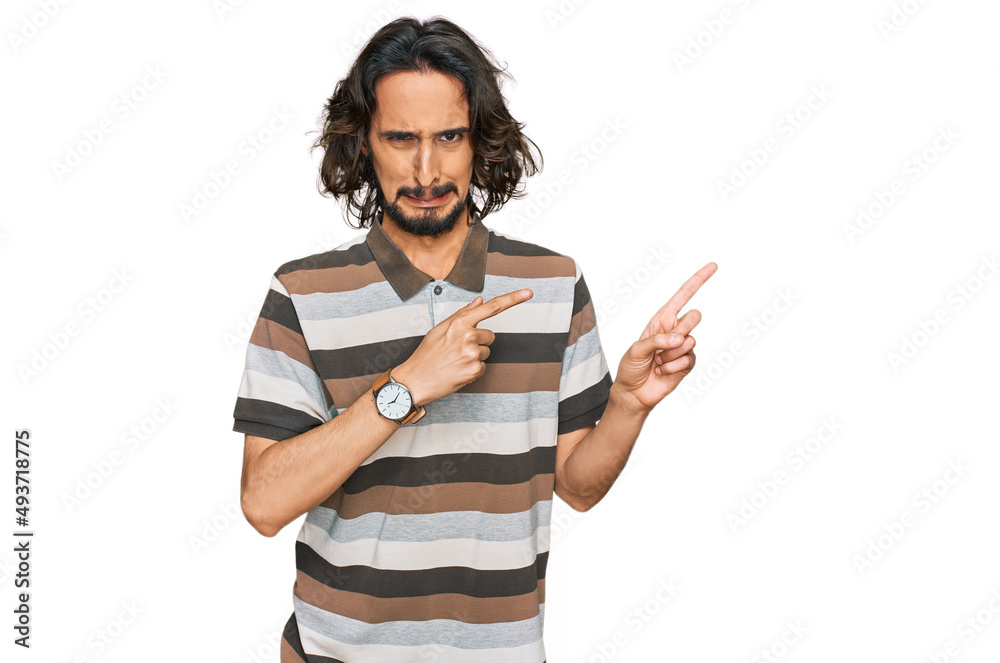 Young hispanic man wearing casual clothes pointing aside worried and nervous with both hands, concerned and surprised expression Young hispanic man wearing casual clothes pointing aside worried and nervous with both hands, concerned and surprised expression