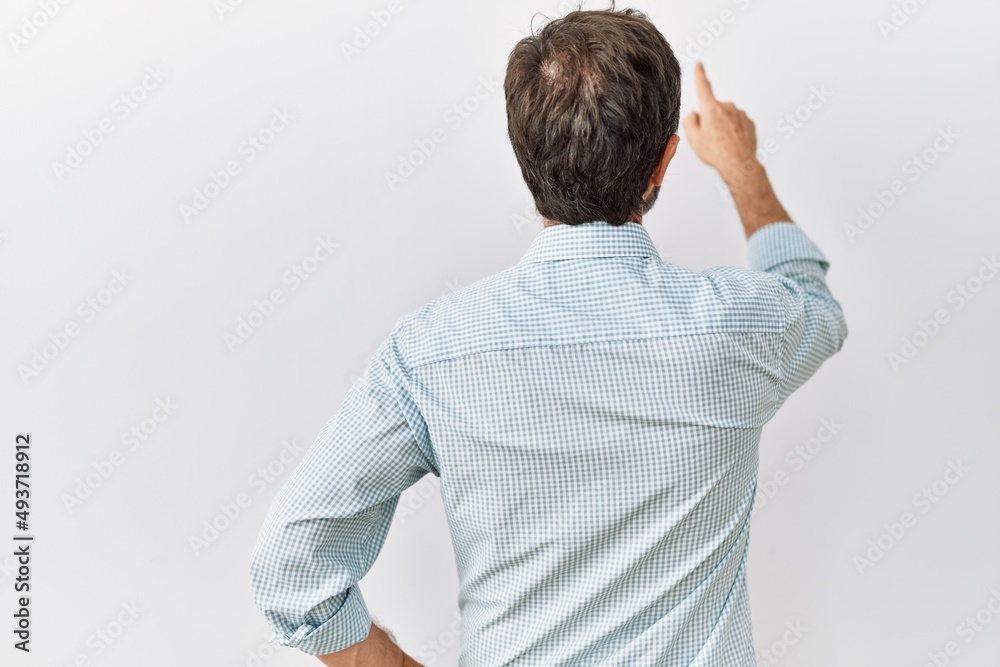 Middle age hispanic man with beard standing over isolated background posing backwards pointing ahead with finger hand Middle age hispanic man with beard standing over isolated background posing backwards pointing ahead with finger hand