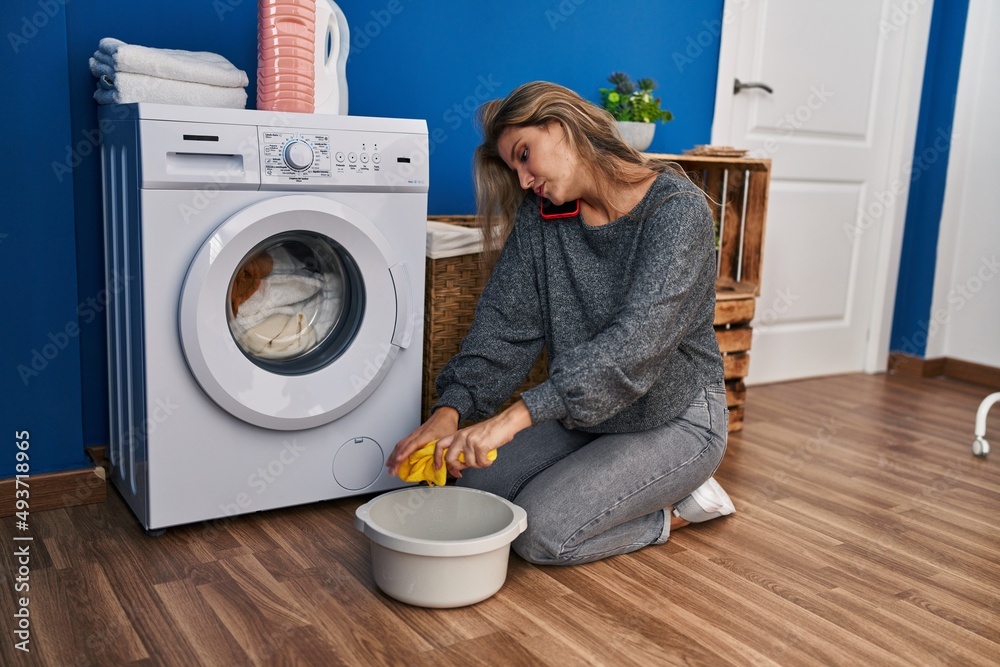 Young blonde woman talking on the smartphone waiting for washing machine at laundry room Young blonde woman talking on the smartphone waiting for washing machine at laundry room