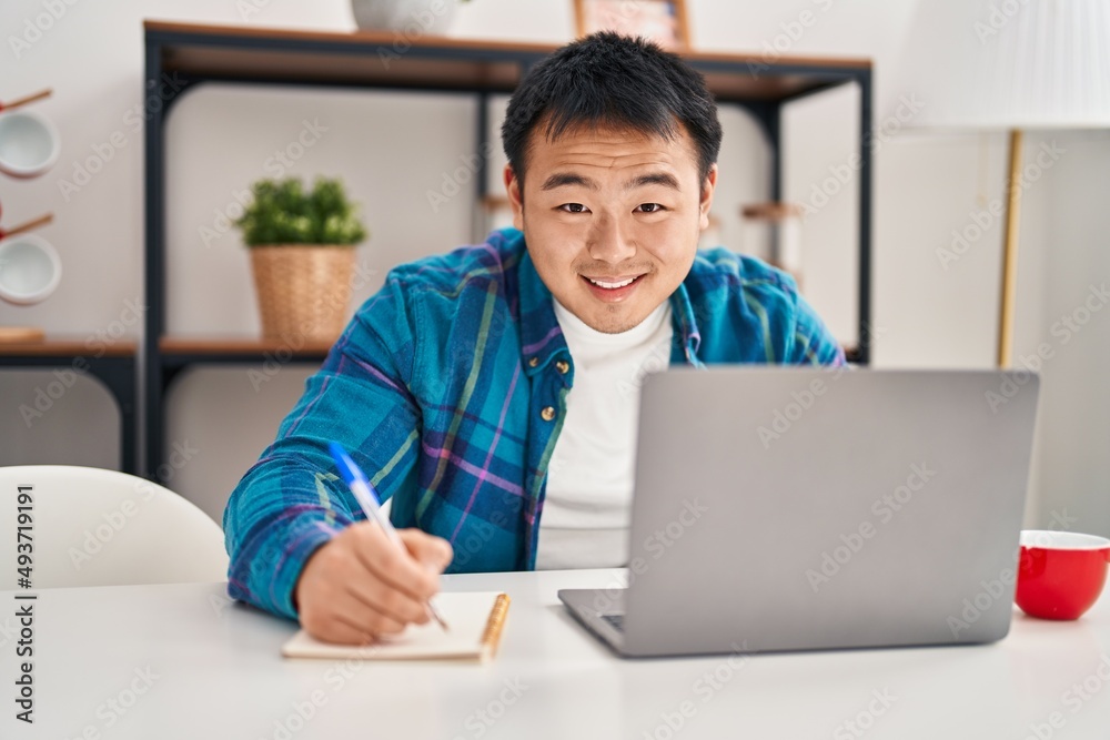 Young chinese man using laptop writing on notebook at home Young chinese man using laptop writing on notebook at home