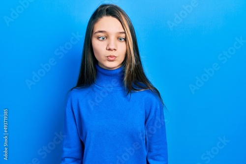 Young brunette girl wearing turtleneck sweater making fish face with lips, crazy and comical gesture. funny expression.