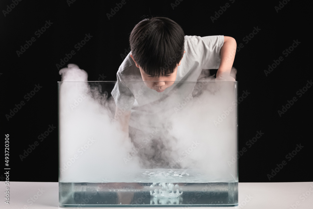 An Asian boy does an experiment with dry Ice or frozen carbon dioxide in the water tank.