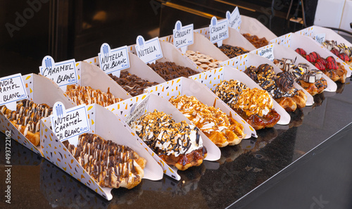 Delicious traditional Liege waffles with colorful toppings on display in a store window in Brussels, Belgium. Sugary desserts. Typical Belgian sweet food.