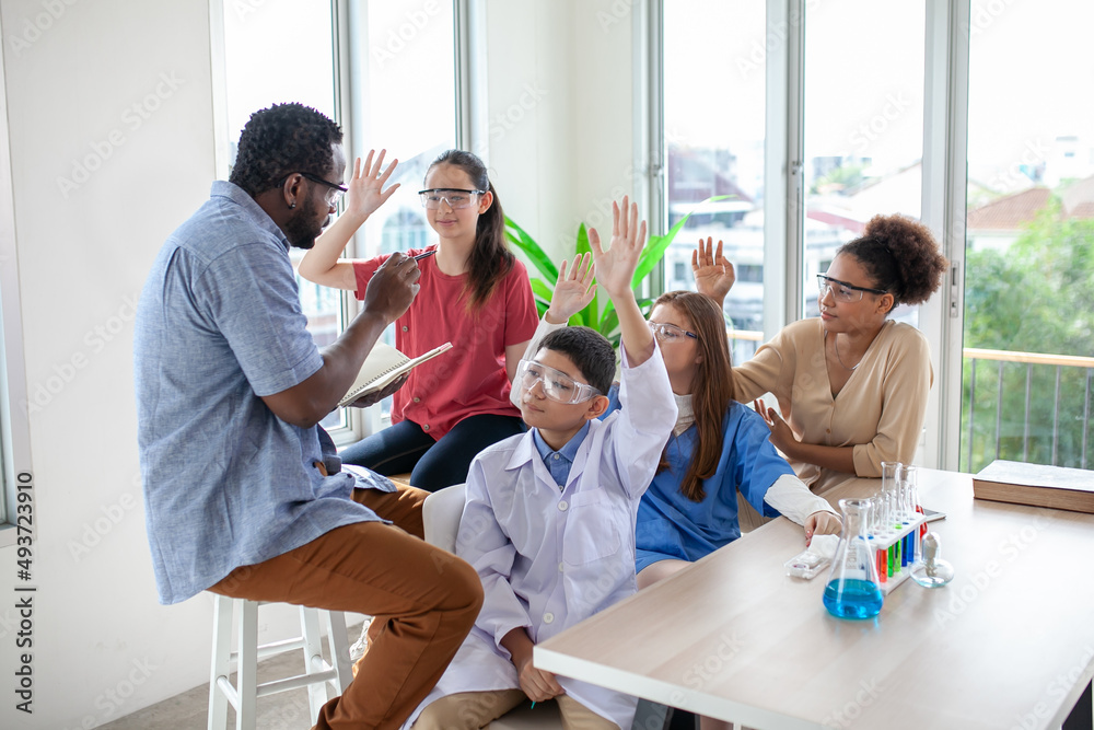 Student raising a hand with a question for the teacher. Teacher pointing at student with hand raised in science classroom. Student raising a hand with a question for the teacher. Teacher pointing at student with hand raised in science classroom.
