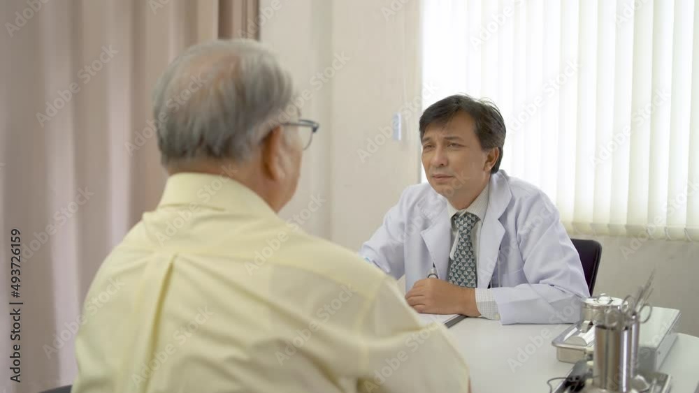 Senior elder man patient talking to caring male doctor physician caregiver at hospital, telling about health check up, disease treatment concept Senior elder man patient talking to caring male doctor physician caregiver at hospital, telling about health check up, disease treatment concept