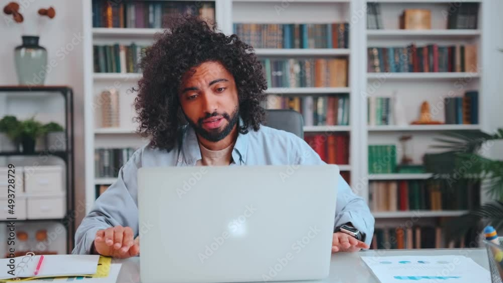 Young excitable Arabian American man fan angry and screaming looking at laptop screen watching game of favorite football team after placing bet on result sits at desk in home office