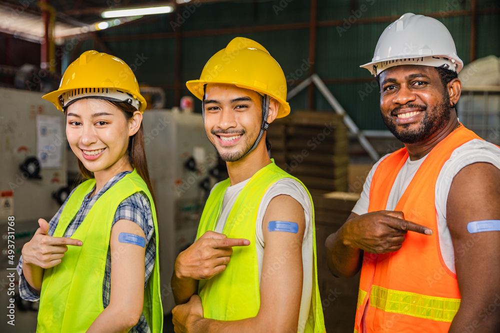 Asian young workers and African man pointing at his arm with a bandage after receiving the covid-19 vaccine.Vaccination for Essential Workers in healthcare at industrial factory.