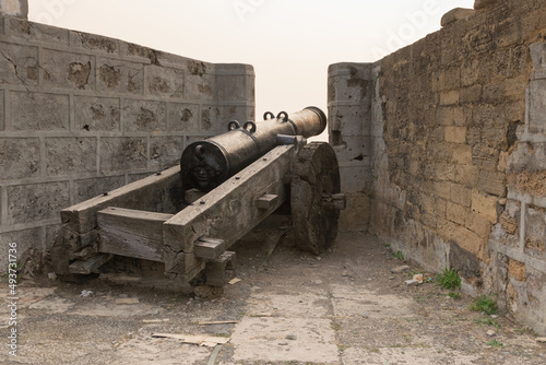 Rear view of a movable sixteenth century Portuguese cannon made of metal with a face design at the back and wooden base. It's located on a bastion of Diu Fort, Diu, India photo