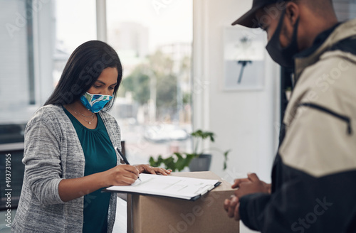 Everything is perfectly in order. Shot of a masked young woman signing for a delivery received at home.