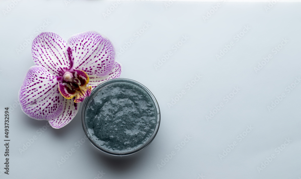 Fototapeta premium natural body or face scrub. olive and clay body polish, sea ebbles, orchid flower. flat layx top biew. spa, wellness and relax concept . skin care. advertising template 