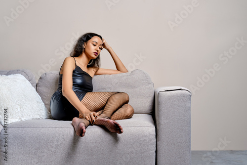 Barefoot african american woman sits with legs tucked on couch