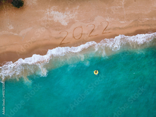 Happy New Year 2022, lettering on the beach with wave and blue sea. Numbers 2022 year on the sea shore, New Years concept.