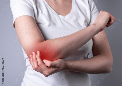 Woman suffering from elbow pain and holding painful hand with red point closeup. Hand injury. Health problems, medicine, treatment concept. High quality photo