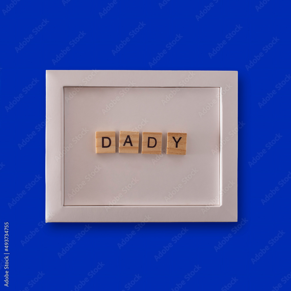 the word DADDY made up of wooden cubes in a white frame on a blue background the word DADDY made up of wooden cubes in a white frame on a blue background