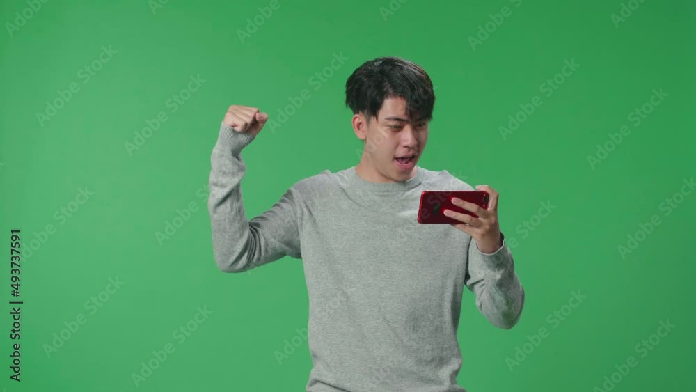 An Asian Man Celebrating After Winning Game On Mobile Phone While Standing In The Green Screen Studio
An Asian Man Celebrating After Winning Game On Mobile Phone While Standing In The Green Screen Studio