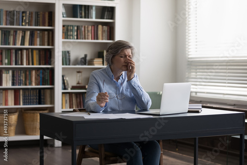 Middle-aged businesswoman sit at desk feels eyestrain takes off glasses rub fatigued eyes Fototapet