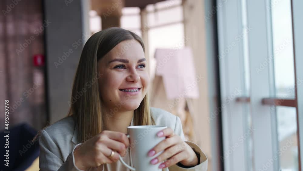 Happy smiling lady enjoys rest and tea during lunch break. Young woman looks dreamily into the window. Happy smiling lady enjoys rest and tea during lunch break. Young woman looks dreamily into the window.