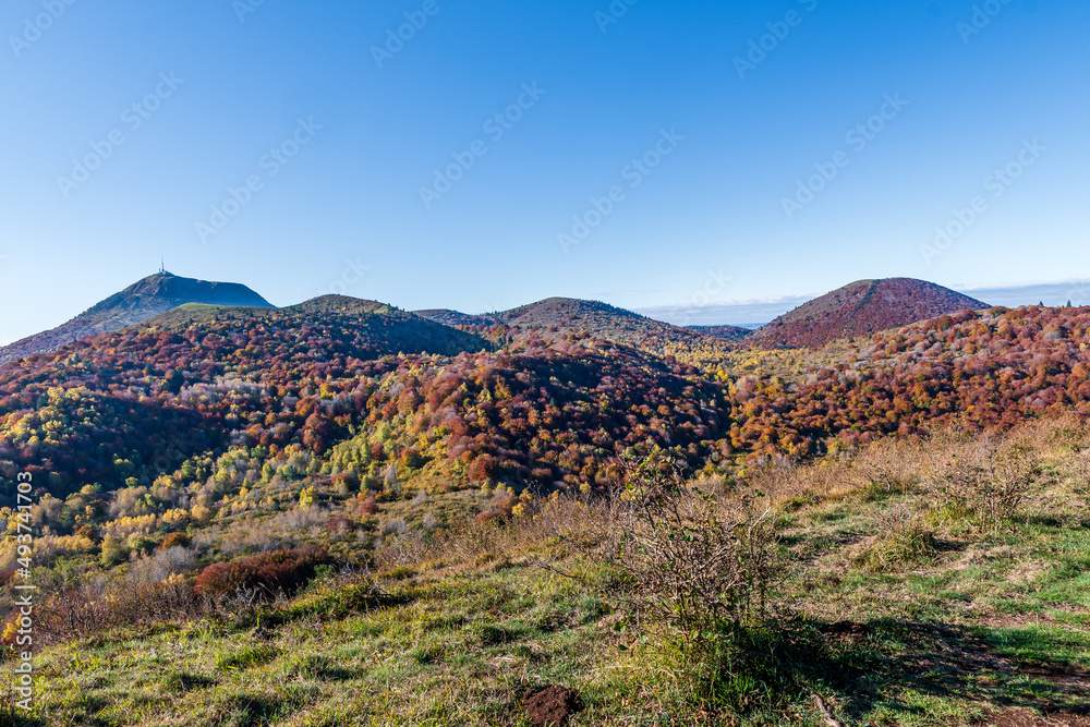 Vue sur une partie du parc des volcans avec tous ces puys recouverts de forets orangées par une belle journée d'automne avec au loin le majestueux puy de dôme