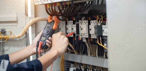 Electrician engineer work tester measuring voltage and current of power electric line in electical cabinet control , concept check the operation of the electrical system .