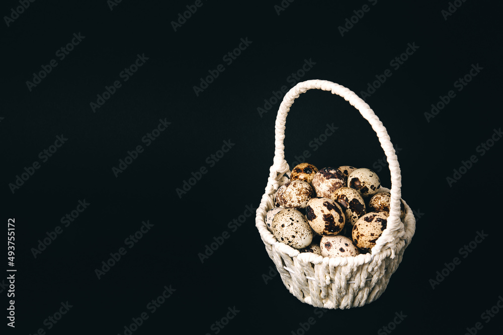 Postcard, white straw basket full of quail eggs on black background. Copy space. Empty text place. Mockup design of Easter holiday. Handmade decor. Healthy food. Visiting card