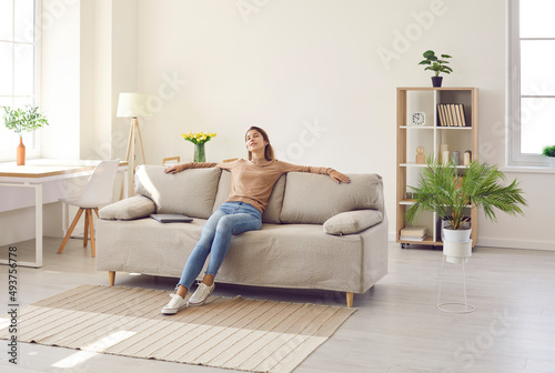 Clam millennial Caucasian girl sit rest on sofa in living room sleep or take nap. Happy young woman relax on comfortable couch furniture at home, daydream doze, relieve negative emotion. Stress free.