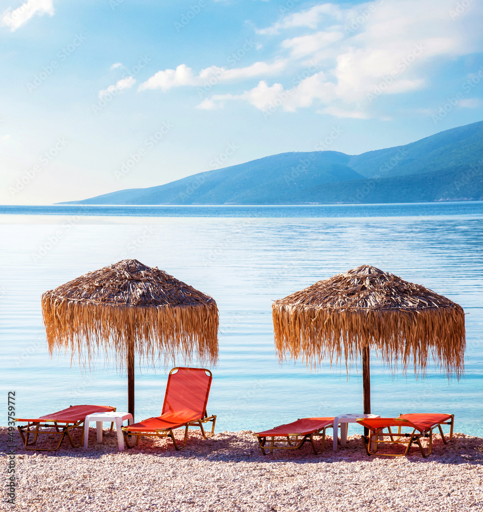 Fabulous landscape with umbrellas and orange sun beds on the seafront on Antisamos Beach on a sunny day on the coast of the Ionian Sea in Kefalonia, Greece. Amazing places. Tourist attractions.