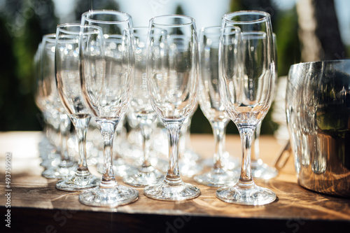 Row of empty champagne glasses on a table outdoors with sun reflection. Selective focus. Celebration concept