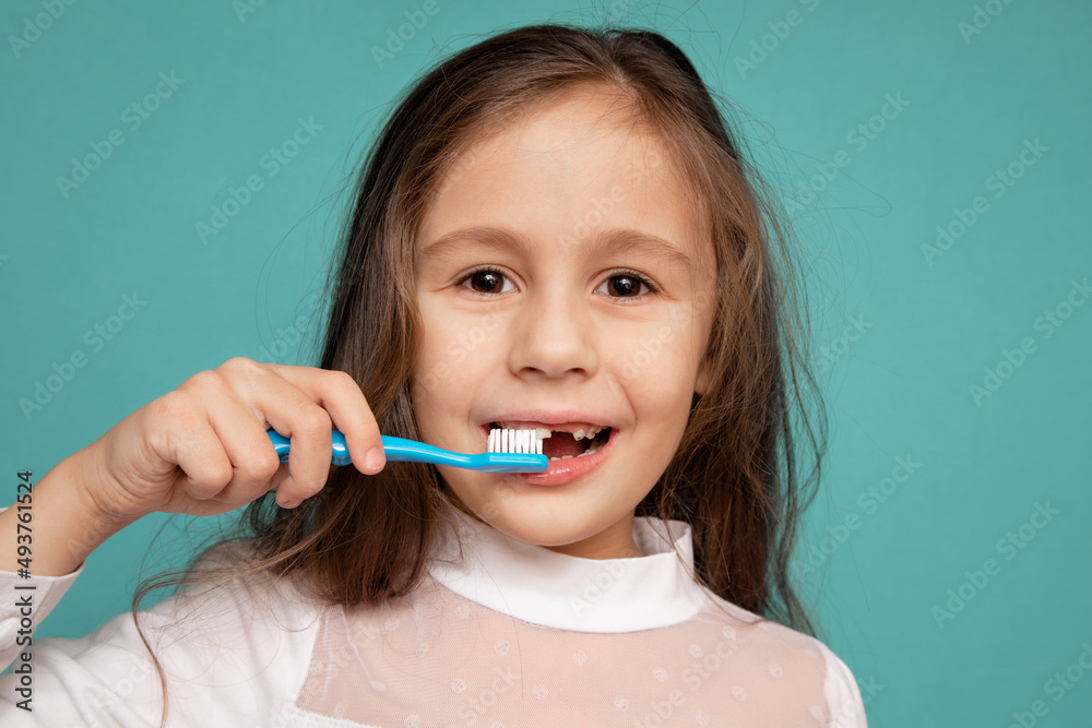 Cute little girl brushing her teeth standing on a blue background Cute little girl brushing her teeth standing on a blue background