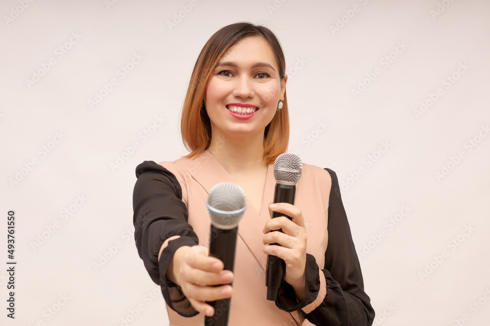 A young woman stands on a white background with a microphone in her hands and invites to speak or sing together while giving a second microphone
