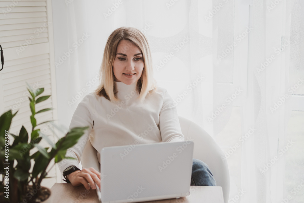 joyful charming woman using laptop and mobile phone smiling while sitting at the workplace joyful charming woman using laptop and mobile phone smiling while sitting at the workplace