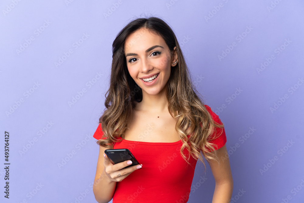 Naklejka premium Young caucasian woman isolated on purple background using mobile phone
