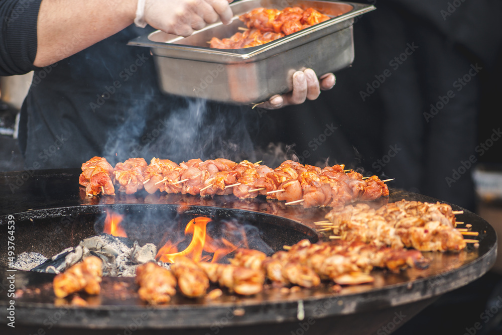 Preparing chicken meat skewers, grilled or roasted in a barbecue on an open fire and flames, shashlik or shashlyk for a picnic with pitchforks, close up