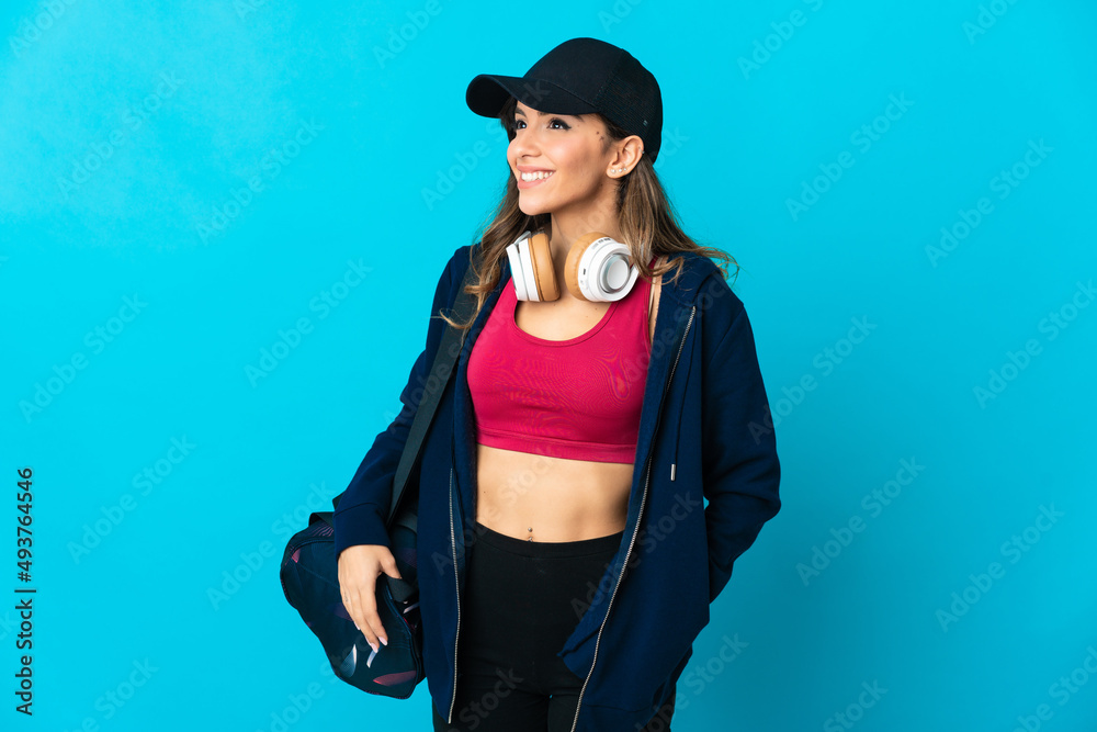 Young sport woman with sport bag isolated on blue background posing with arms at hip and smiling