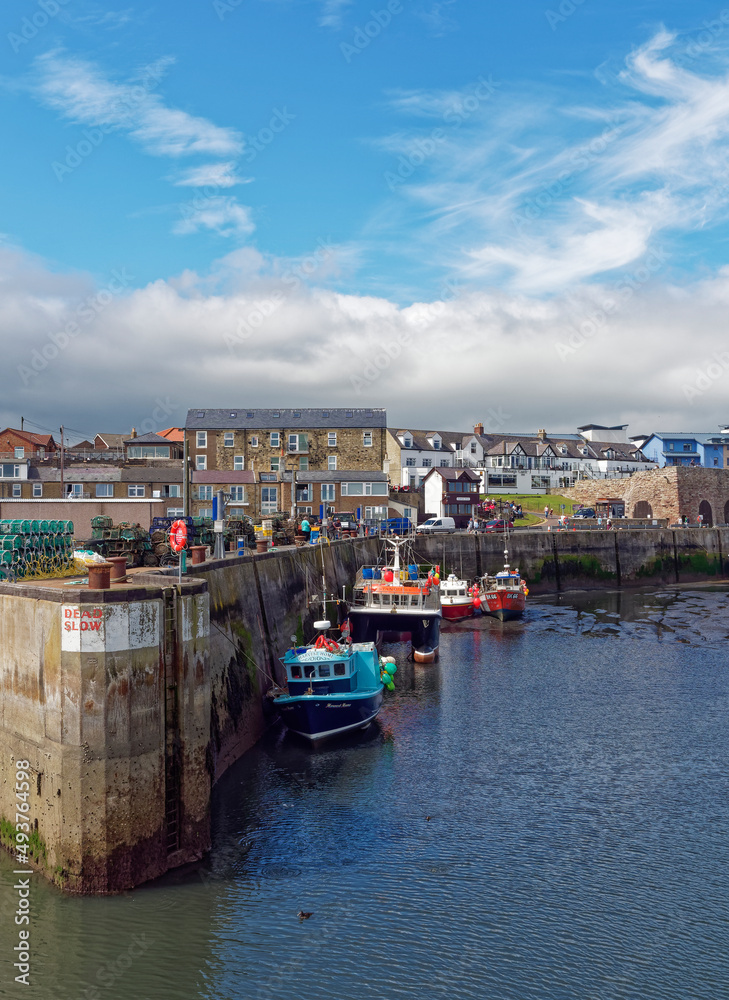 Seahouses  Harbour at Low Tide, with Boats resting on the silty bottom of the Harbour, overlooked by Houses and Commercial Buildings.