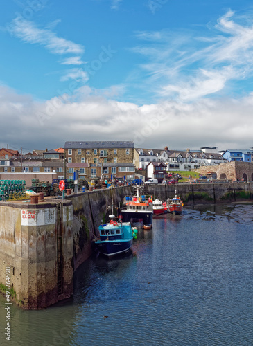 Seahouses Harbour at Low Tide, with Boats resting on the silty bottom of the Harbour, overlooked by Houses and Commercial Buildings.