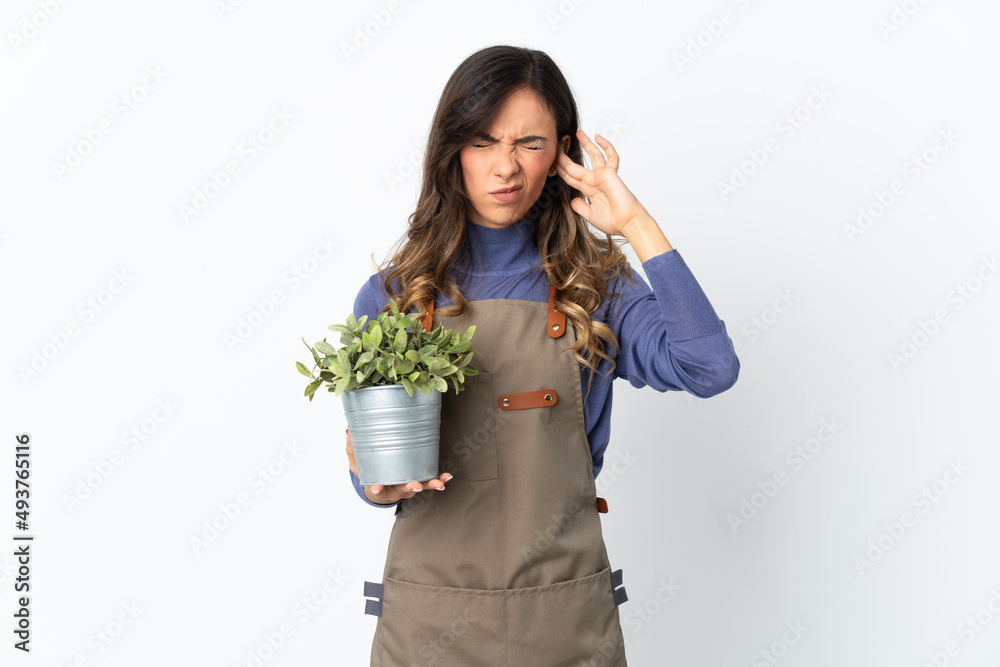 Gardener girl holding a plant isolated on white background frustrated and covering ears