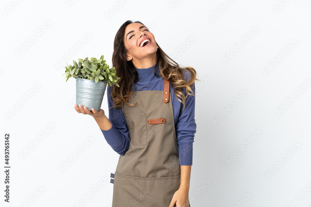 Gardener girl holding a plant isolated on white background laughing Gardener girl holding a plant isolated on white background laughing