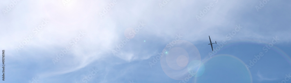 A glider plane in blue cloudy sky low angle photography.As banner with lens flare. A glider plane in blue cloudy sky low angle photography.As banner with lens flare.