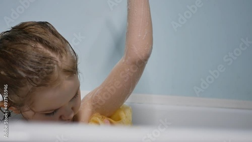 Portrait. a little preschooler takes a bath on her own, soaps herself with a washcloth while sitting in the bath. Slow motion, close up