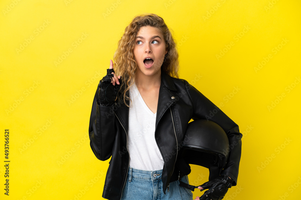 Young blonde woman with a motorcycle helmet isolated on yellow background thinking an idea pointing the finger up Young blonde woman with a motorcycle helmet isolated on yellow background thinking an idea pointing the finger up