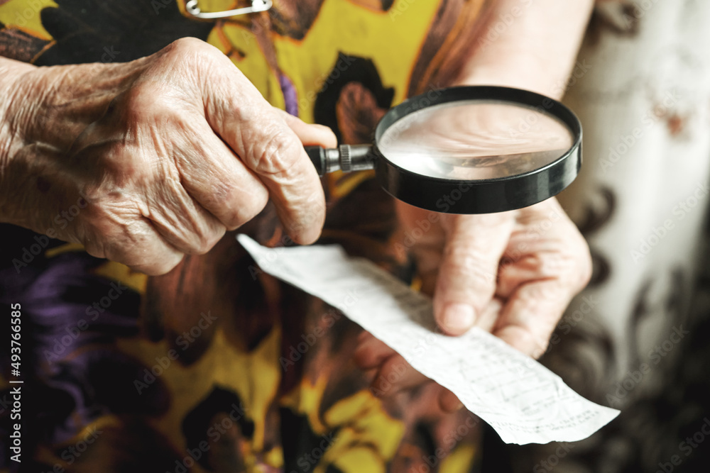 elderly woman uses a magnifying glass to read through the lens of a bank account