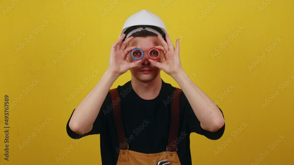 Funny smiling electrician in hardhat holds insulating tape in his hands. Electrician posing on yellow background Funny smiling electrician in hardhat holds insulating tape in his hands. Electrician posing on yellow background